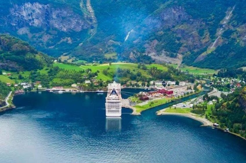 Ein Kreuzfahrtschiff in einem Fjord, umgeben von Bergen und einer kleinen Stadt. 4