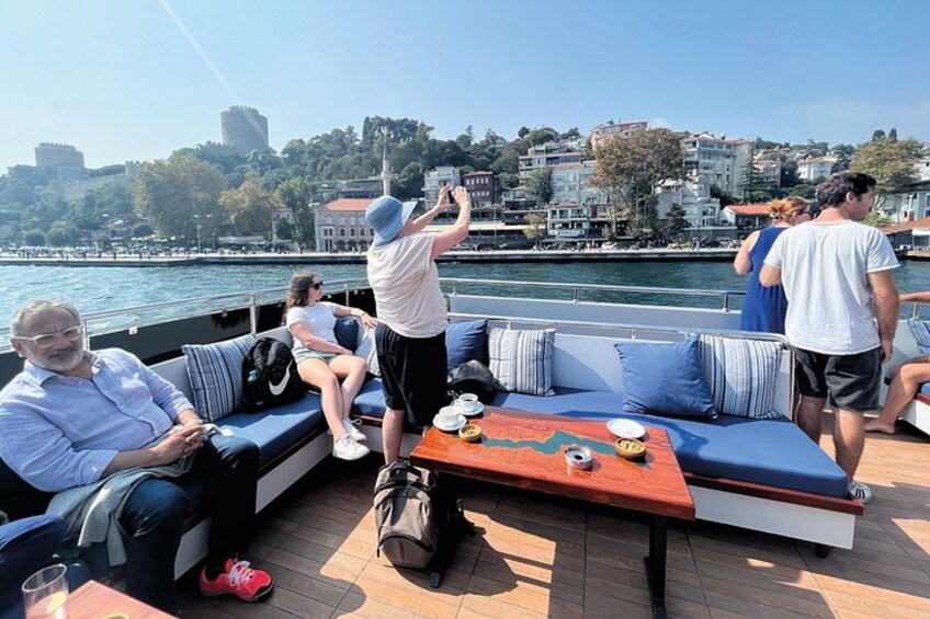 A boat with people sitting and standing, a table with food, and a cityscape in the background. 2