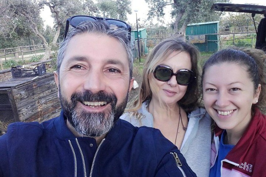 Three people outdoors with a wooden structure and greenery in the background. 2