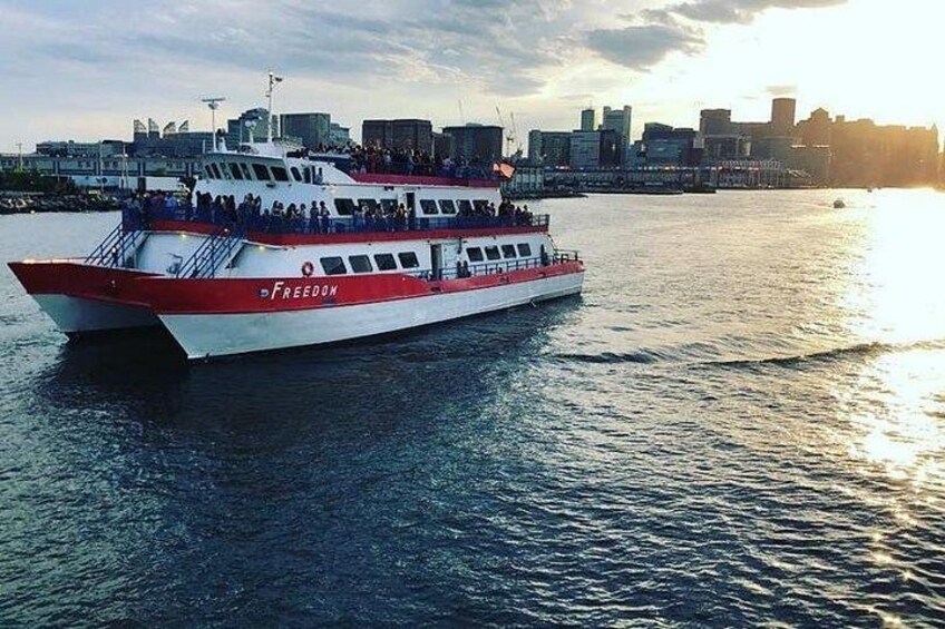Un ferry llamado 'Freedom', con pasajeros, navegando por un río con el horizonte de una ciudad al fondo. 1