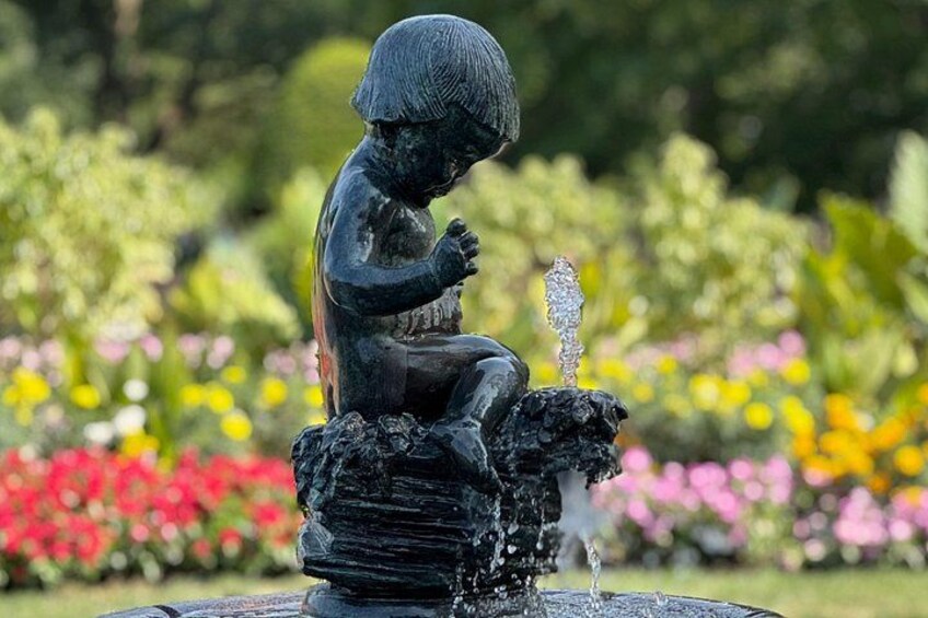 En staty som föreställer ett barn som sitter vid en fontän i en trädgård. 5