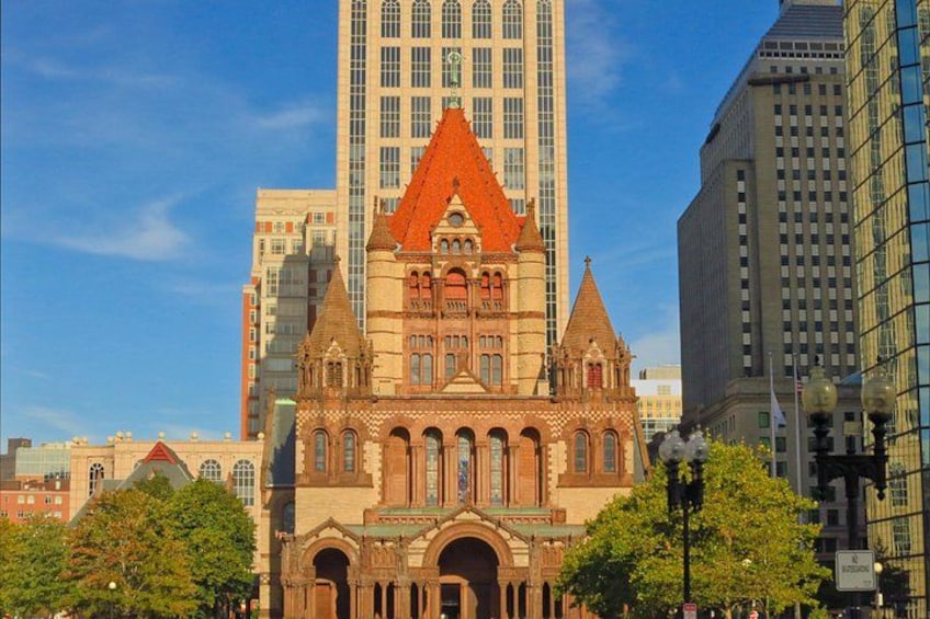 A historic building with a red roof and arched windows, surrounded by modern high-rise buildings. 1