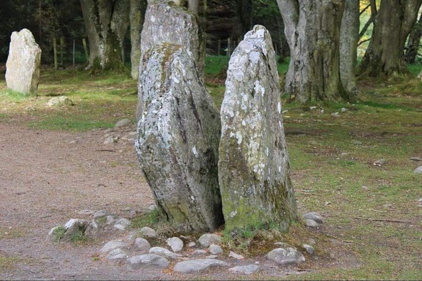 Two standing stones in a forested area with a dirt path and a fence in the background. 3