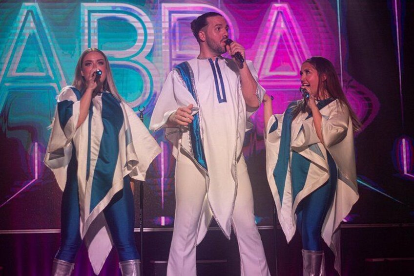 Three people on stage with microphones, wearing white outfits with blue accents. 5