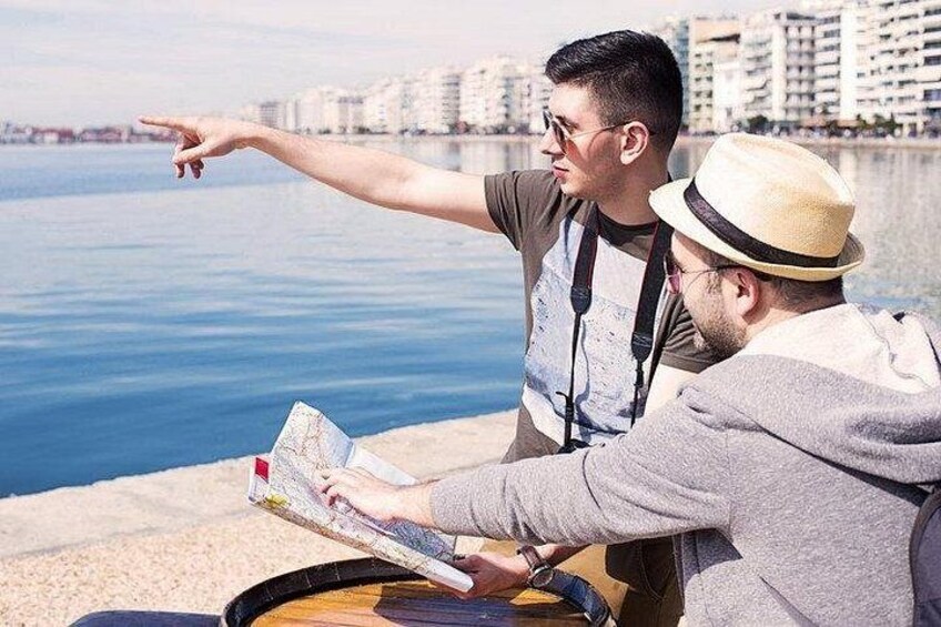 Two people sitting by a waterfront, one pointing towards the water, and the other looking at a map. 1