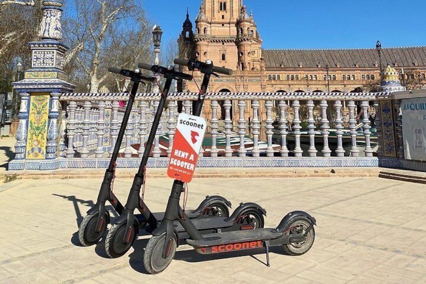 Deux trottinettes électriques Scoonet sont garées devant un bâtiment historique orné de balustrades décoratives. 5