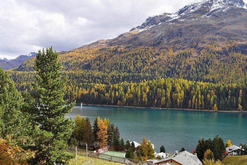 A lake surrounded by forested mountains, a clear sky, and residential buildings. 5