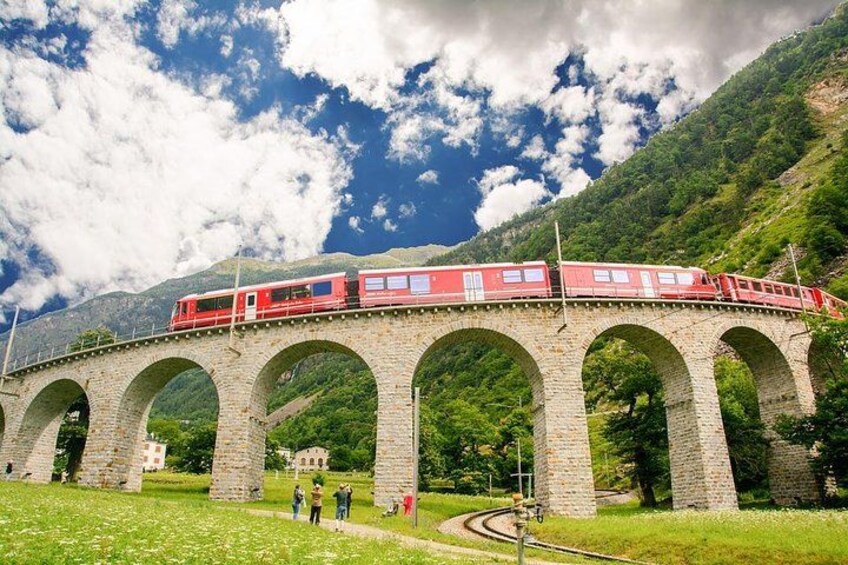 Un train rouge sur un pont de pierre à arcades, entouré de verdure et de montagnes. 2