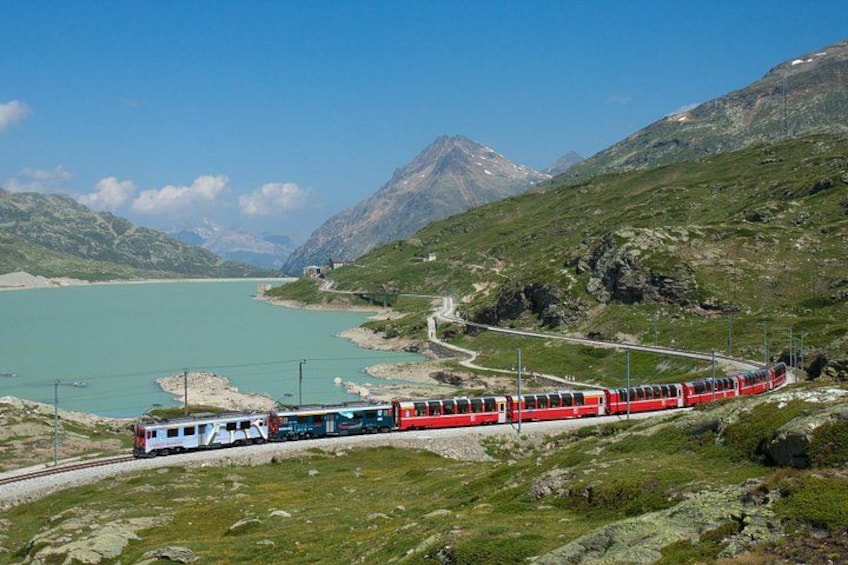 A red train traveling through a mountainous landscape with a lake. 1