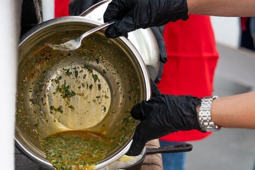 A person wearing black gloves stirring a pot with a spoon. 4