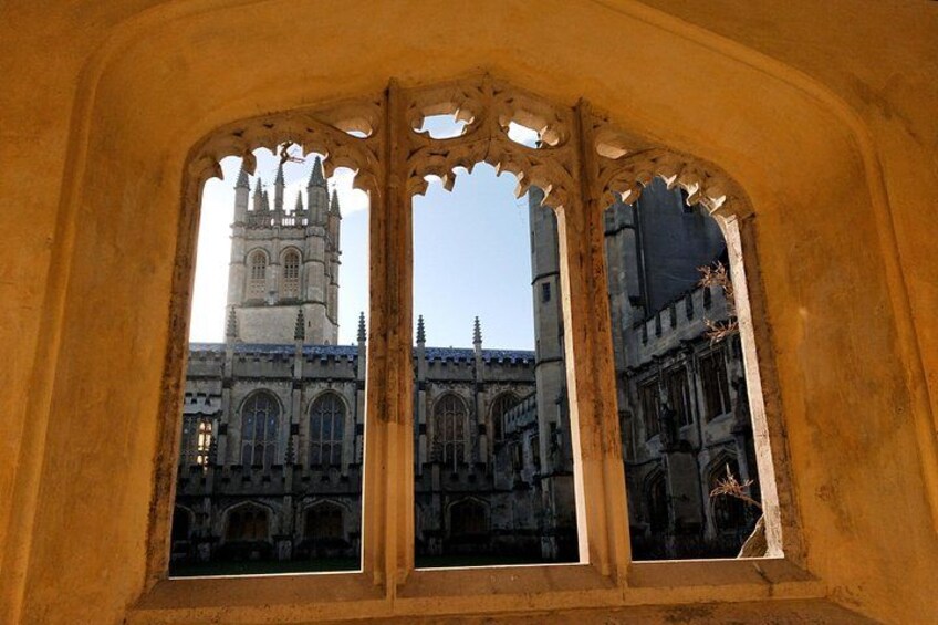 Une fenêtre gothique ornée de motifs complexes et offrant une vue sur une cathédrale surmontée d’une haute flèche. 3
