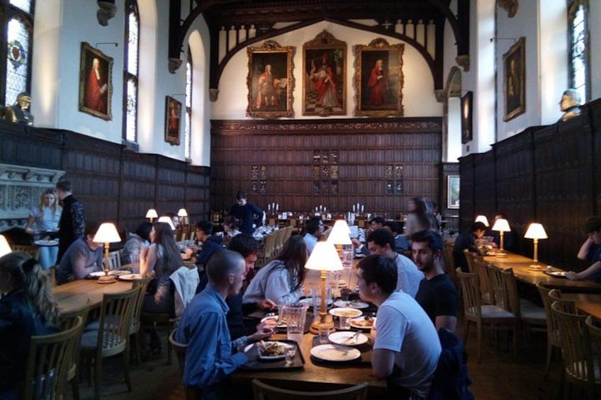 Une salle à manger avec des tables et des chaises en bois, des personnes qui mangent et des tableaux accrochés aux murs. 1