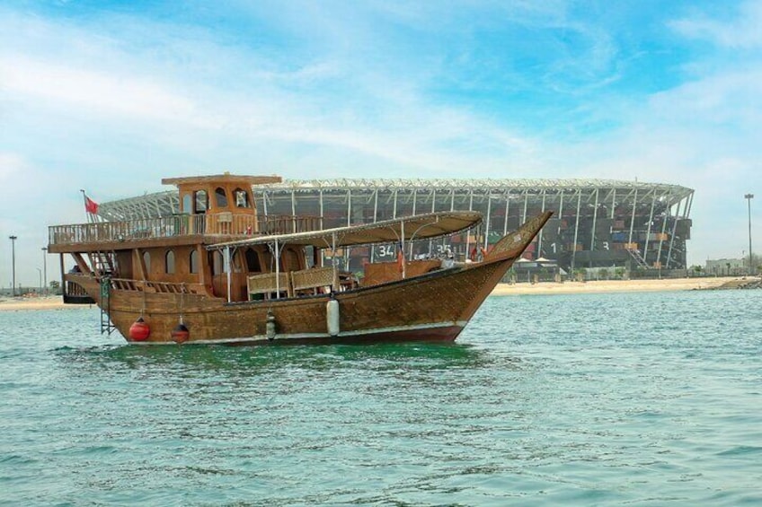 Un’imbarcazione di legno tradizionale sull'acqua, con un moderno stadio sullo sfondo. 1
