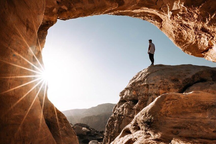 A person standing on a rock formation with a sun shining through an arch. 2