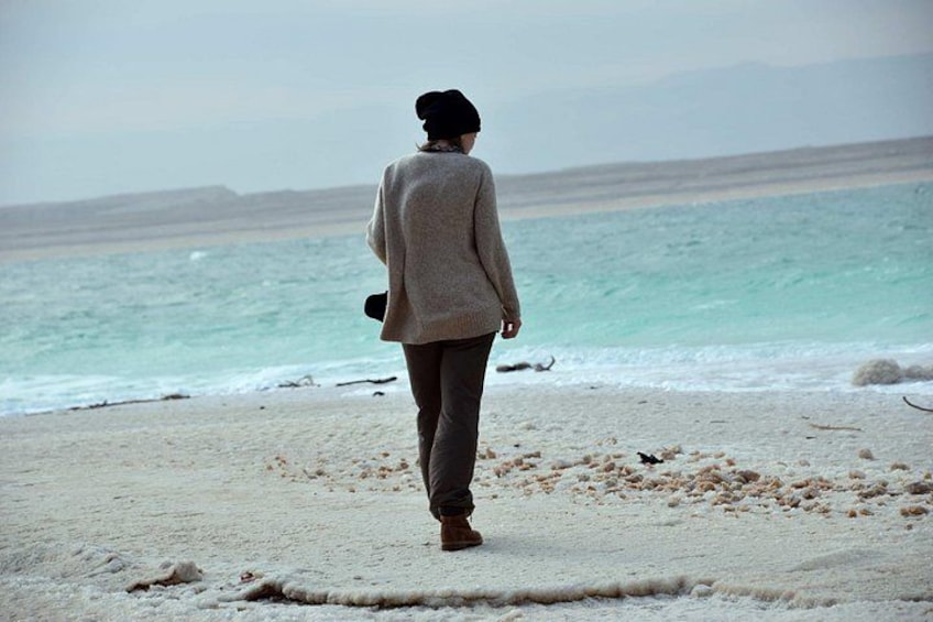 A person walking on a beach with a calm sea and distant mountains. 5