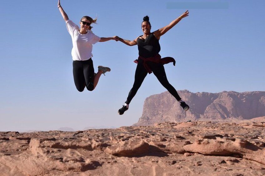 Two people jumping in a desert landscape with rocky terrain and mountains in the background. 3
