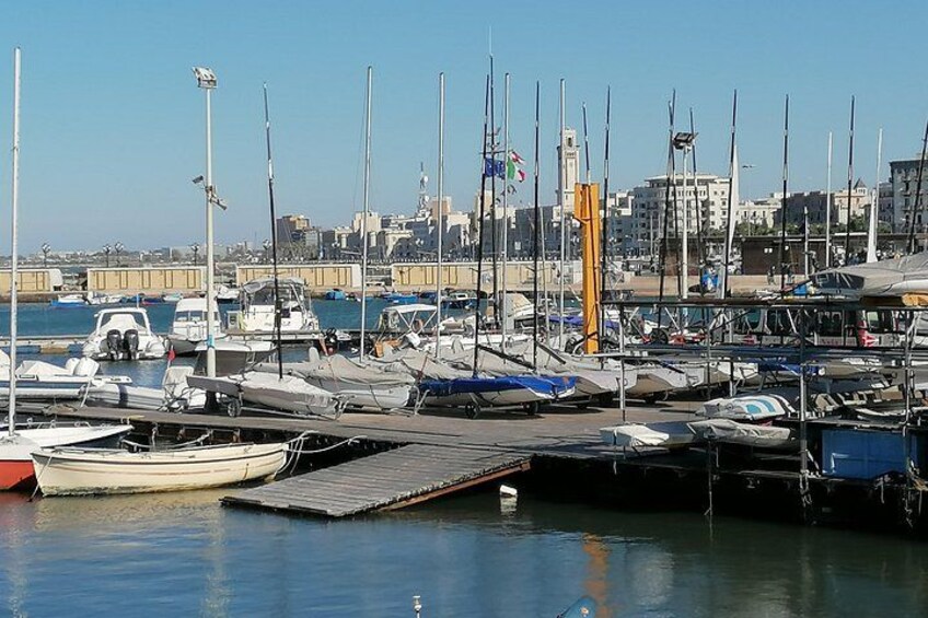Een jachthaven met diverse boten afgemeerd, met een stadsgezicht op de achtergrond en een heldere lucht. 2
