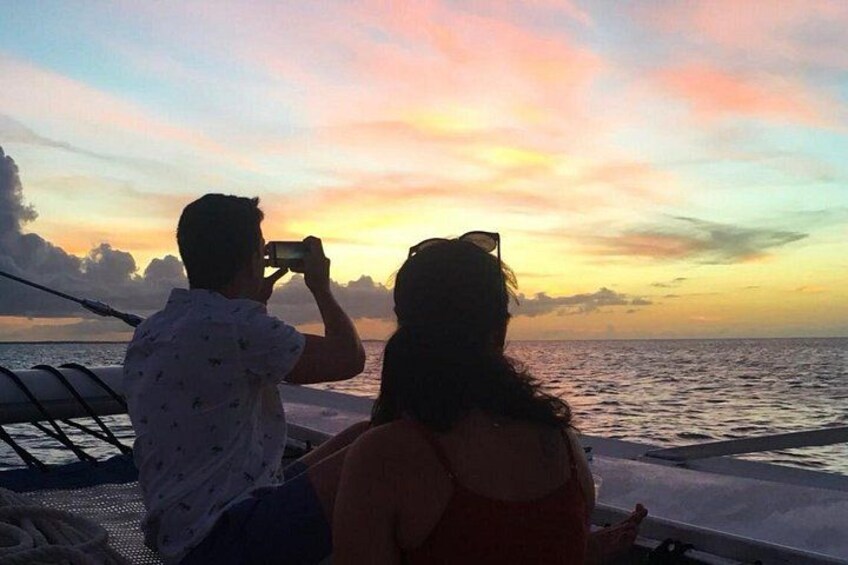 Two people on a boat, one taking a photo, with a sunset in the background. 2
