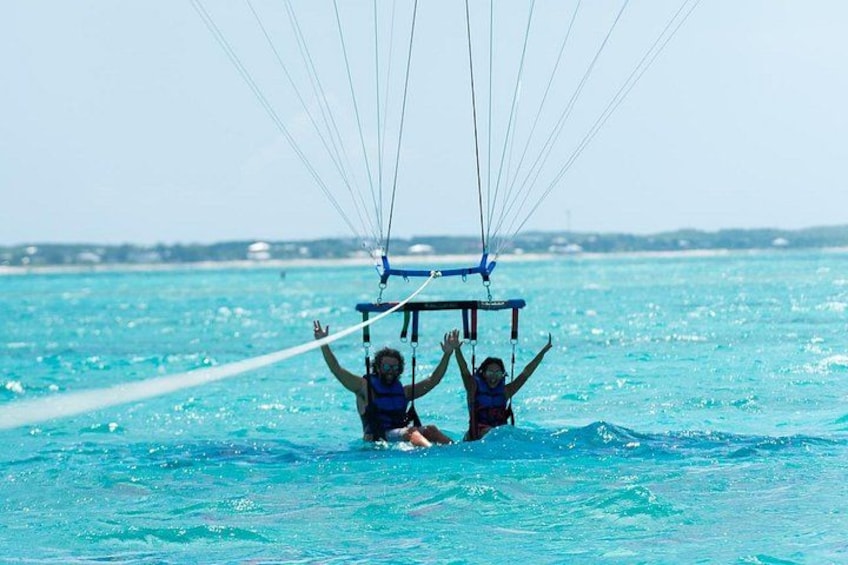 Dos personas haciendo parasailing sobre aguas turquesas bajo un cielo despejado. 1