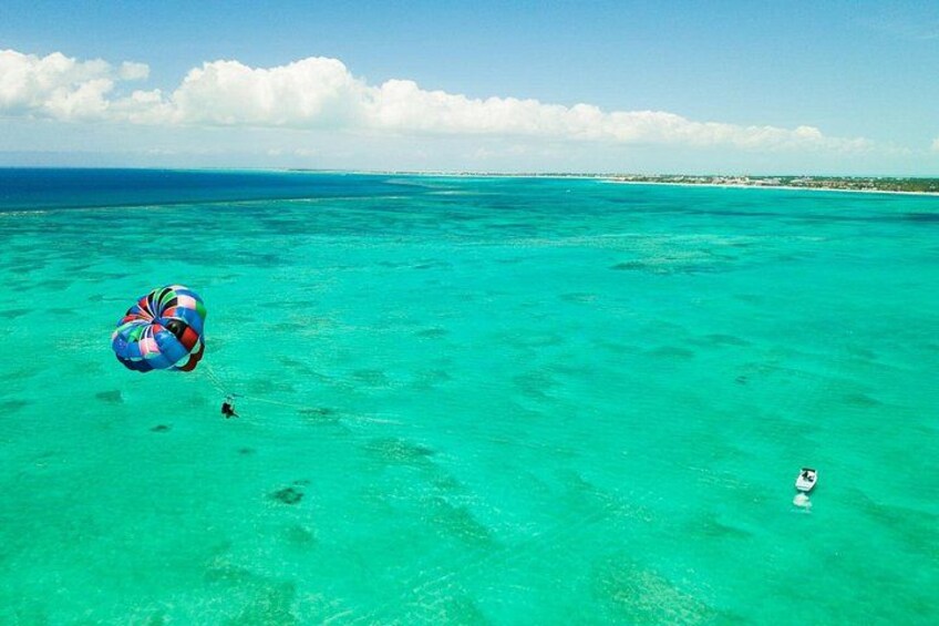 A person parasailing over turquoise ocean waters with a clear sky. 2