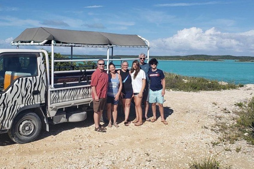 A group of people standing in front of a vehicle with a zebra print design, near a body of water with a clear sky. 1