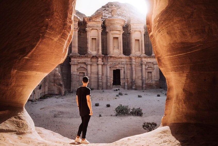 A person standing between two rock formations, looking at an ancient building. 3