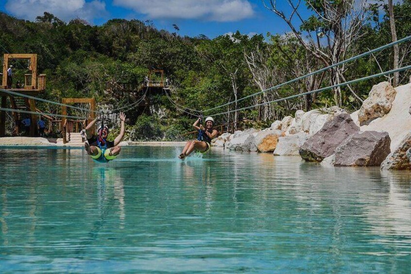 People on a zip line over a body of water with a forested background. 3