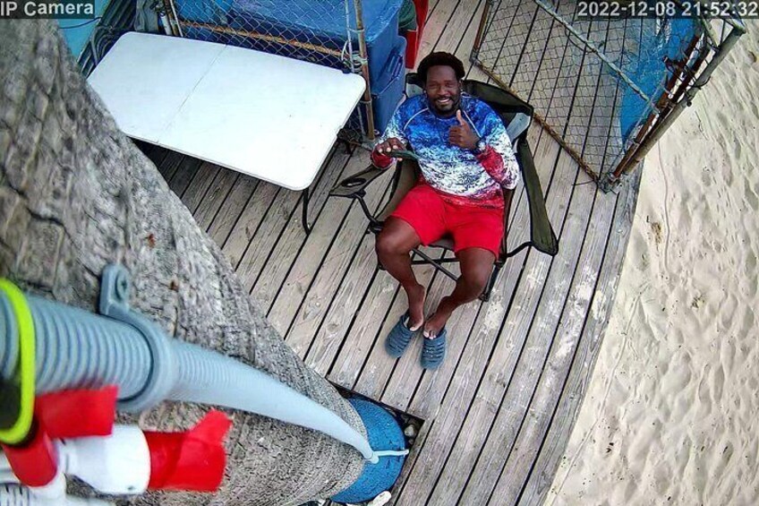 A person sitting on a chair on a wooden deck with a white object and a blue object nearby. 4