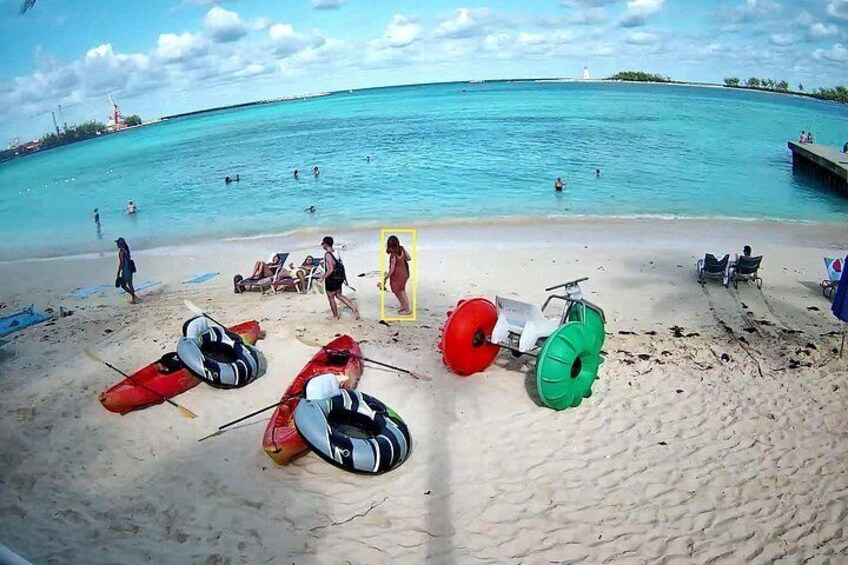 A beach with clear turquoise water, people swimming, and various watercraft like kayaks and a jet ski. 3