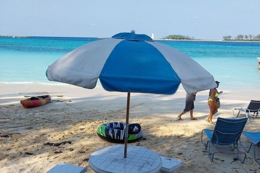 A beach with a blue and white umbrella, a kayak, and beach chairs. 5