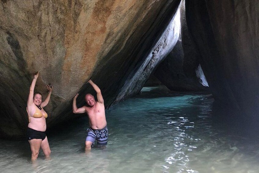 Dos personas de pie en aguas poco profundas bajo una gran formación rocosa. 1