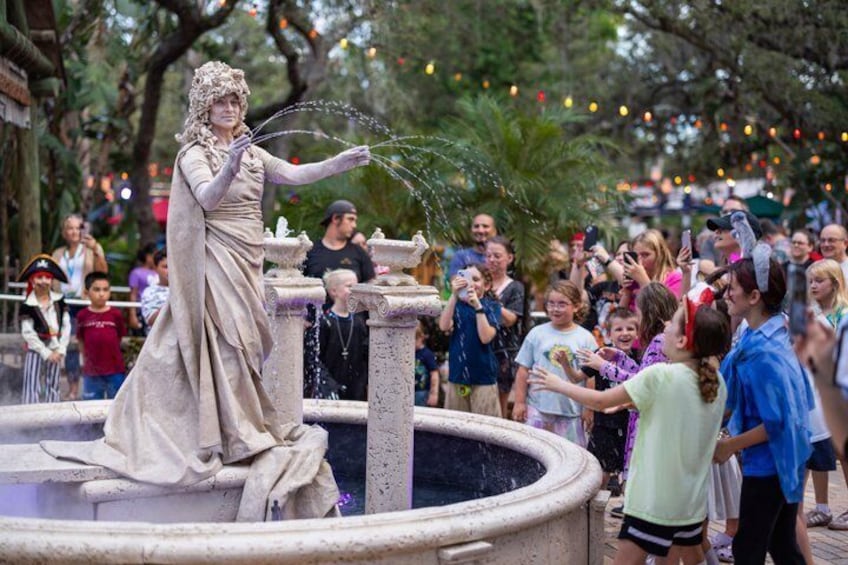 A statue of a woman in a dress spraying water from her hands, surrounded by a crowd of people. 3
