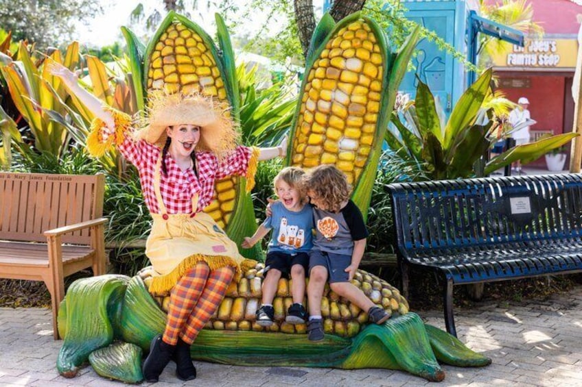A person in a corn cob costume with two children sitting on a corn cob sculpture. 5