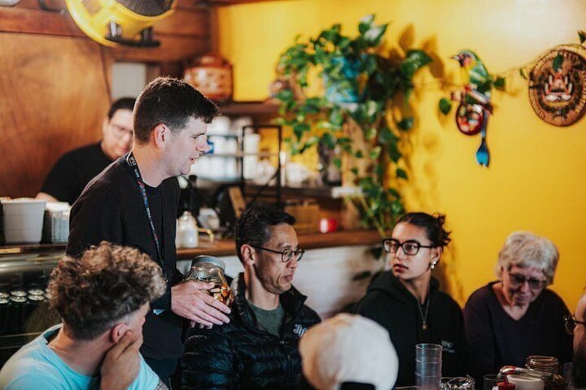 A group of people in a restaurant with a yellow wall and plants. 2