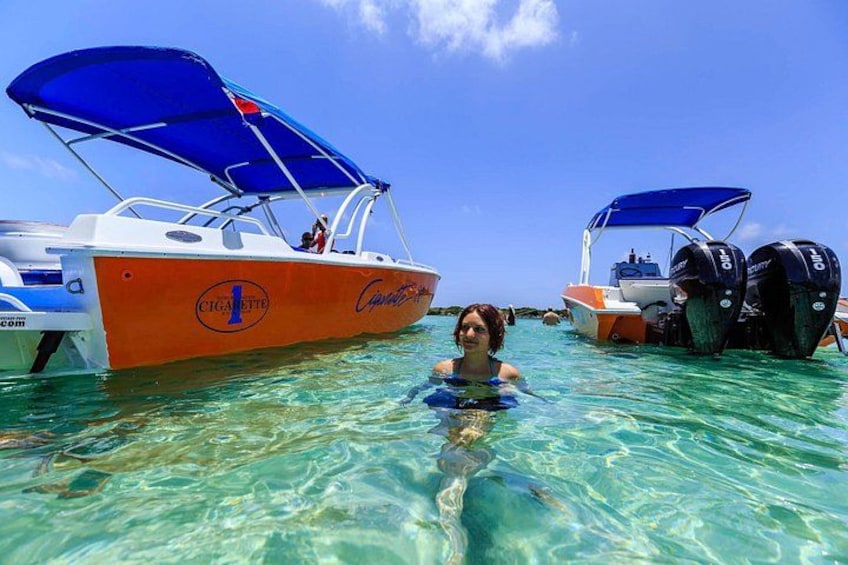 A person swimming in clear turquoise water with two boats in the background. 5