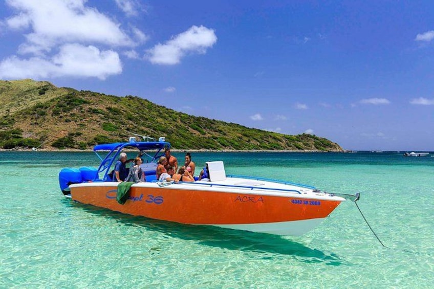 A boat with people on it, clear turquoise water, and a hilly landscape in the background. 2