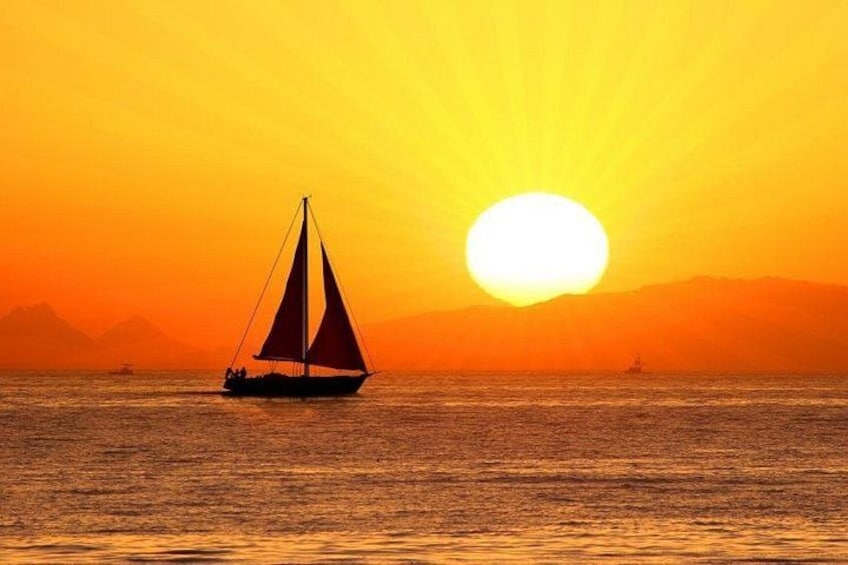 A sailboat on calm waters during sunset with a sun low on the horizon and mountains in the background. 1