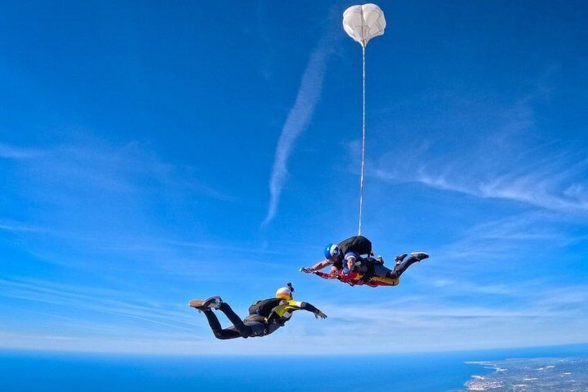 Two skydivers in freefall with a parachute above them. 2