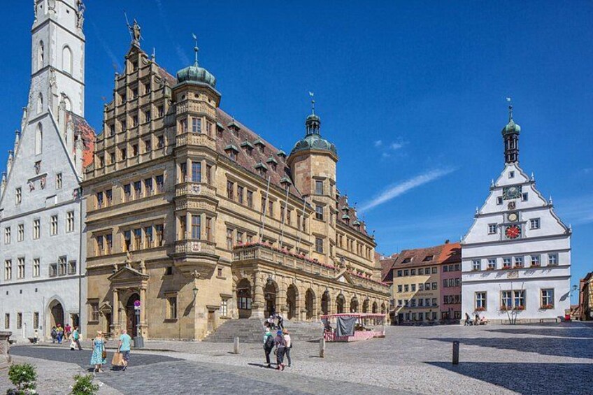 A historic European square with ornate buildings, a clock tower, and a cobblestone street. 1