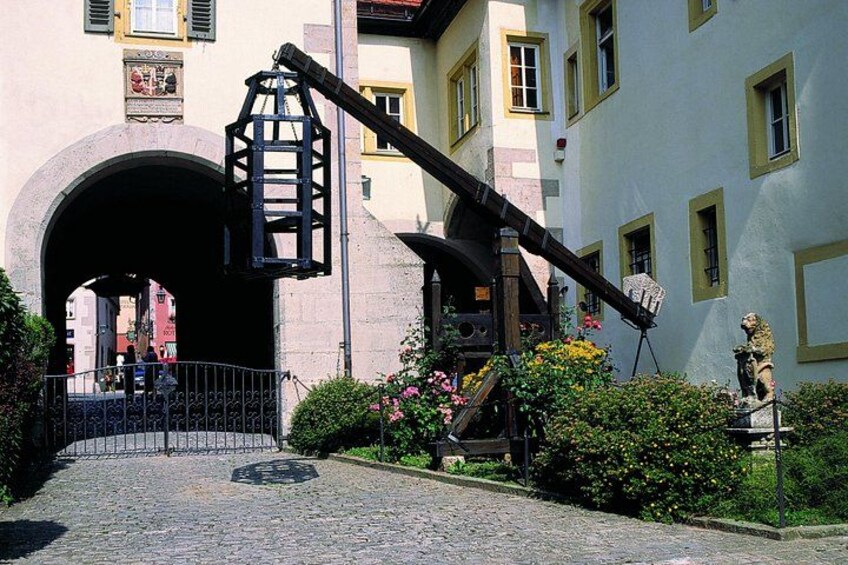 A cobblestone street leading to a historic building with a large arched entrance, a black metal lantern, and a statue. 5