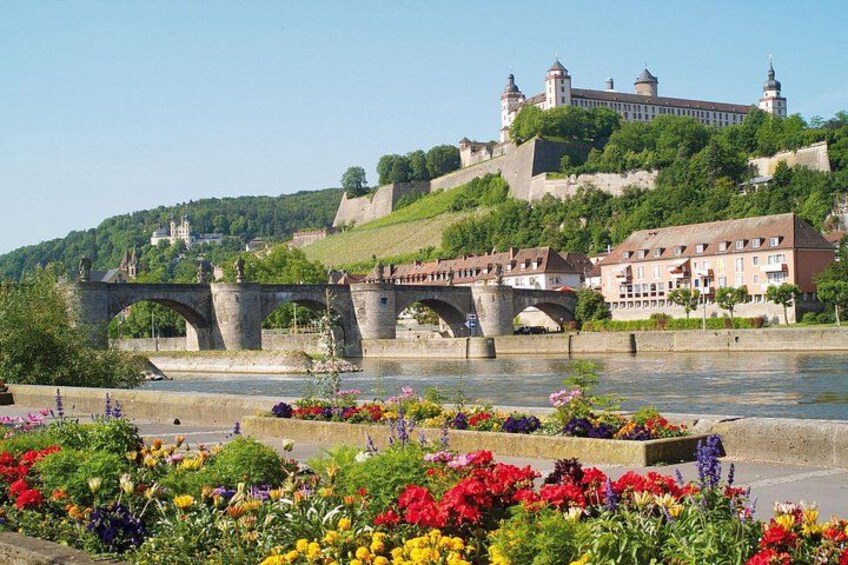 A river with a bridge, colorful flower beds, and a castle on a hill. 3
