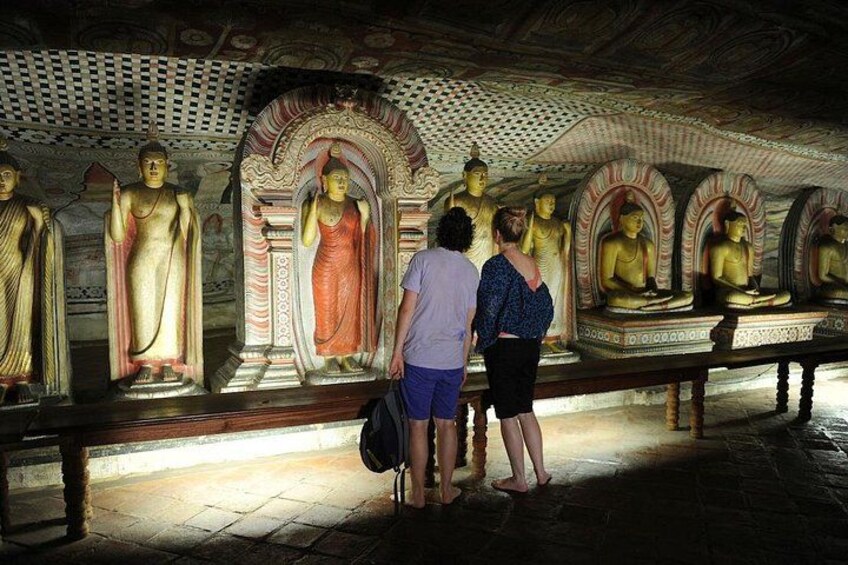 Tempelinteriør med gyldne Buddha-statuer, besøgende der betragter dem, og et detaljeret loft. 2