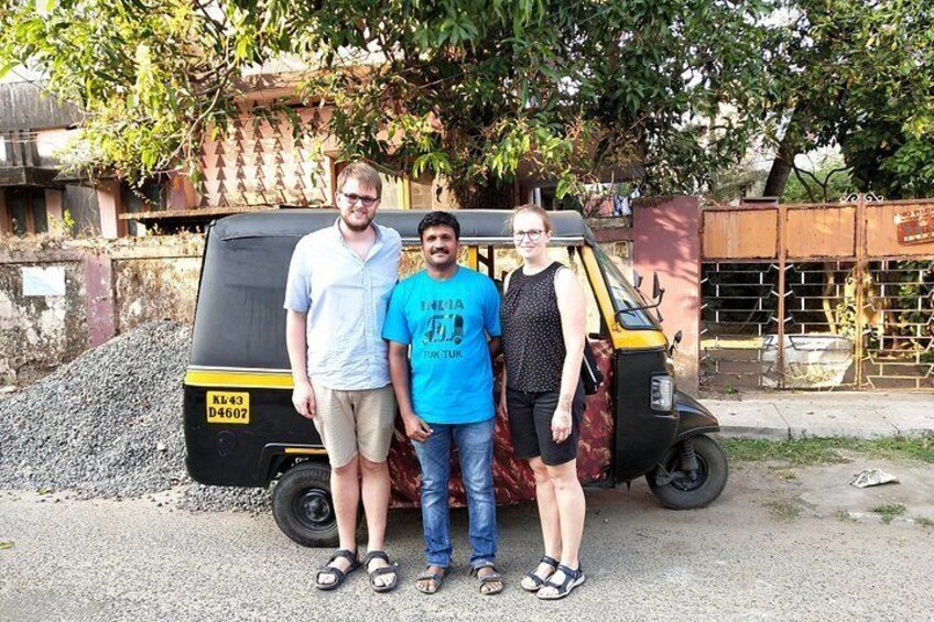 Three people standing in front of a black auto-rickshaw with a yellow license plate. 2