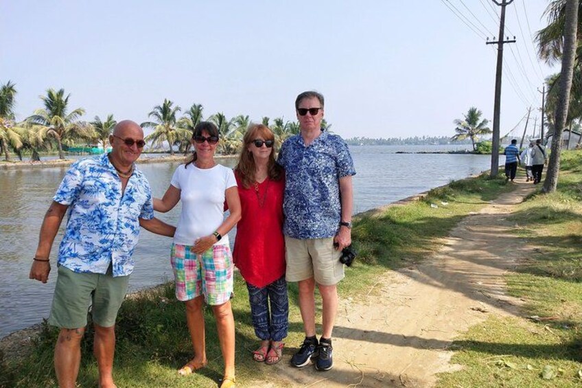 A group of people standing by a water body, a dirt path, and palm trees in the background. 2