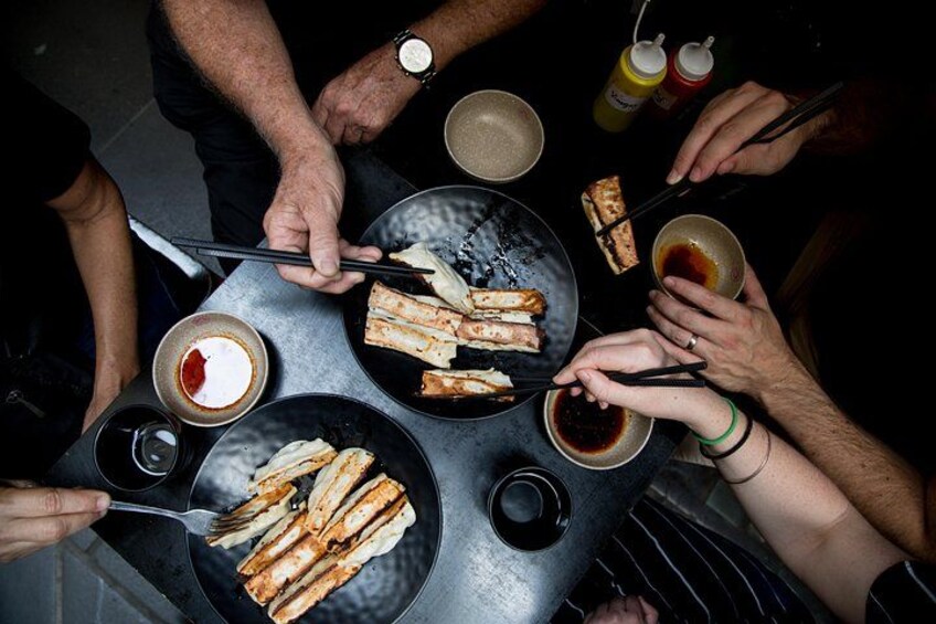 Mensen eten aan een tafel, met stokjes, schalen met saus en borden vol eten. 1