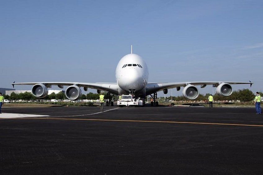 A large airplane on the tarmac with ground crew in safety vests. 3