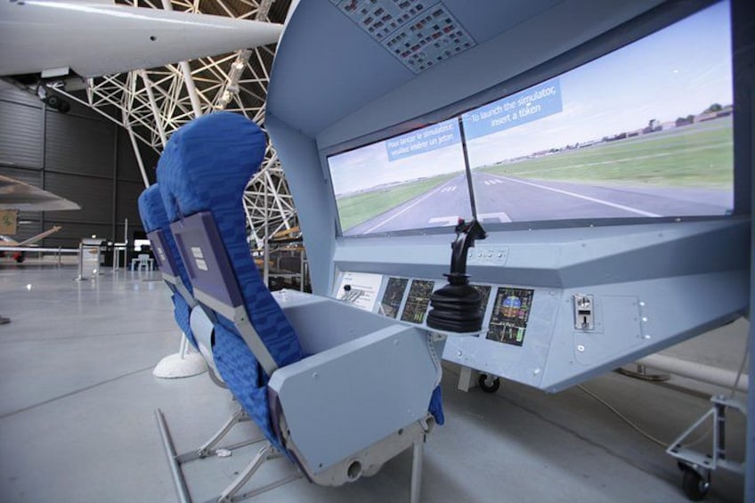 A flight simulator cockpit with a large screen displaying a runway, control panels, and a blue chair. 2