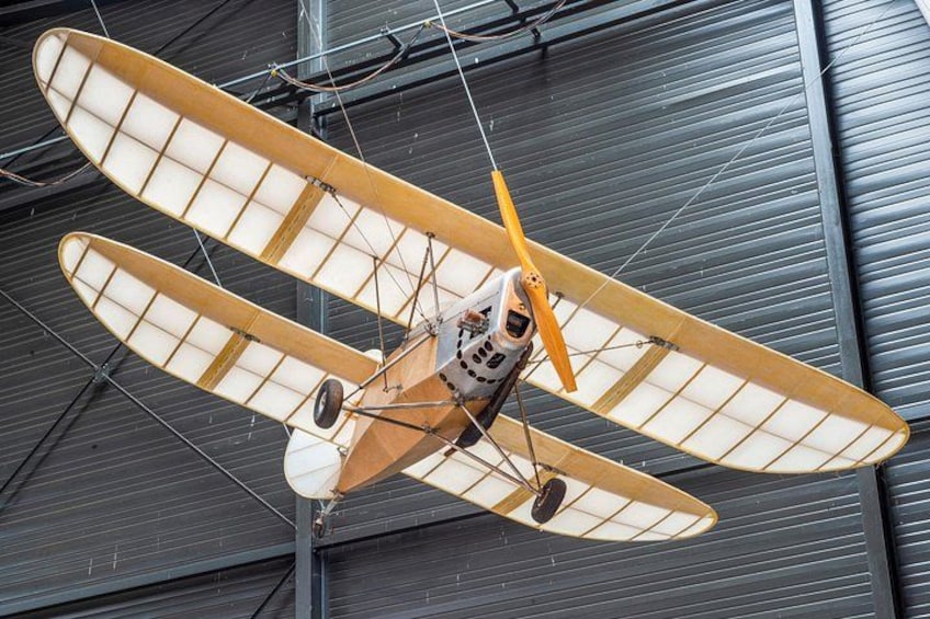 A vintage biplane with two wings, suspended in a hangar. 5
