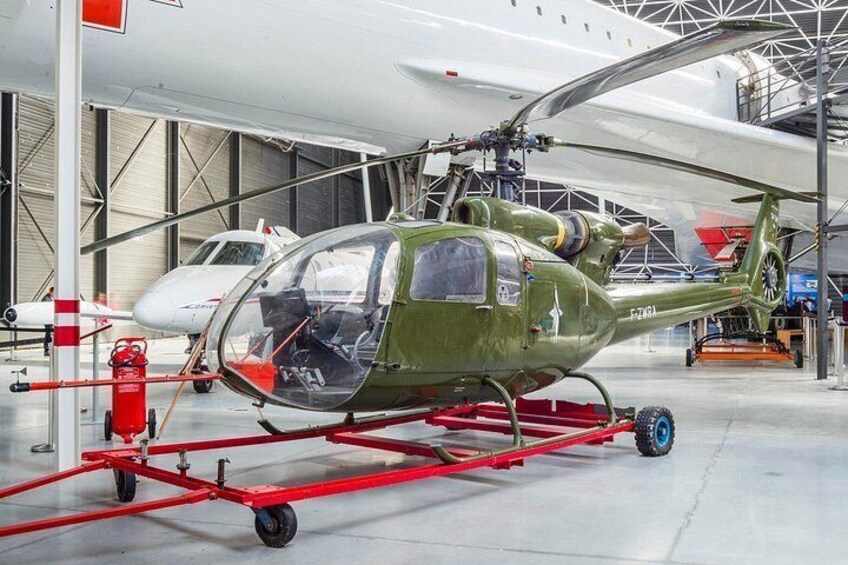 A green helicopter with a red frame, parked indoors with other aircraft in the background. 4