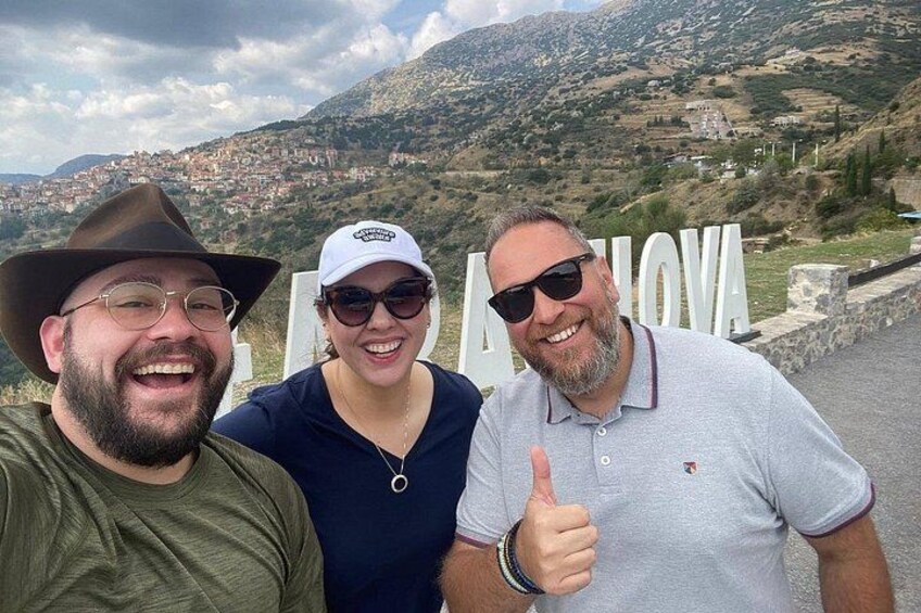 Three people posing in front of a sign with the word 'ALBONA' and a mountainous landscape in the background. 4